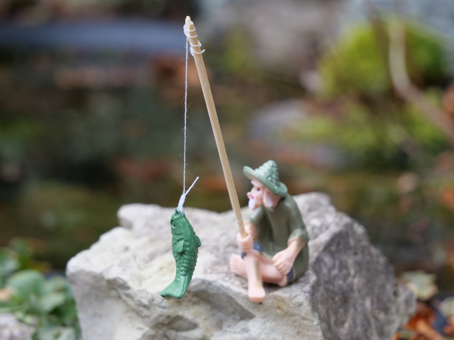 Nahaufnahme eines grünen Fisches an der Angel, Teil einer dekorativen Fischerfigur für Miniteiche und Gartenlandschaften