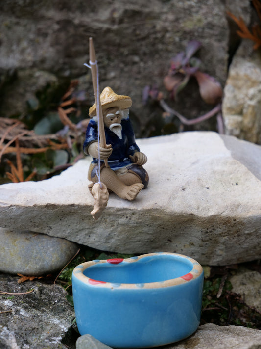 Sitzende Fischerfigur aus Keramik mit blauer Kleidung, Angelrute und gefangenem Fisch, dekorative Miniteich- und Gartendeko
