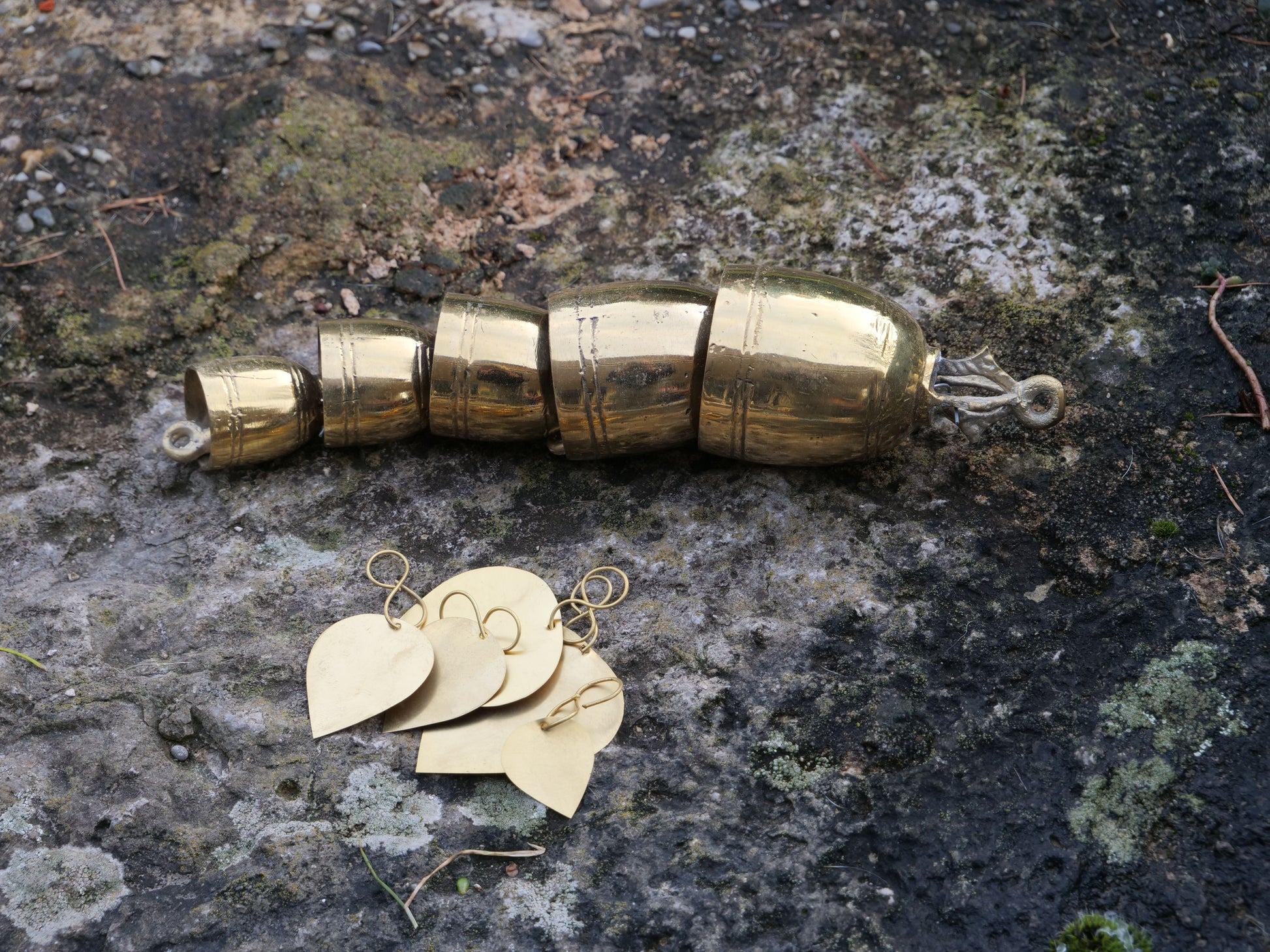 Messing-Glöckchen-Set auf einem Stein, bestehend aus mehreren gestaffelten Glocken und herzförmigen Anhängern.