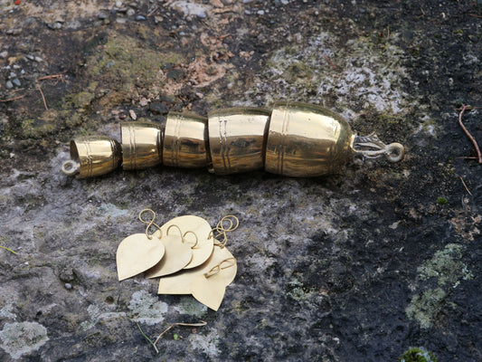 Messing-Glöckchen-Set auf einem Stein, bestehend aus mehreren gestaffelten Glocken und herzförmigen Anhängern.