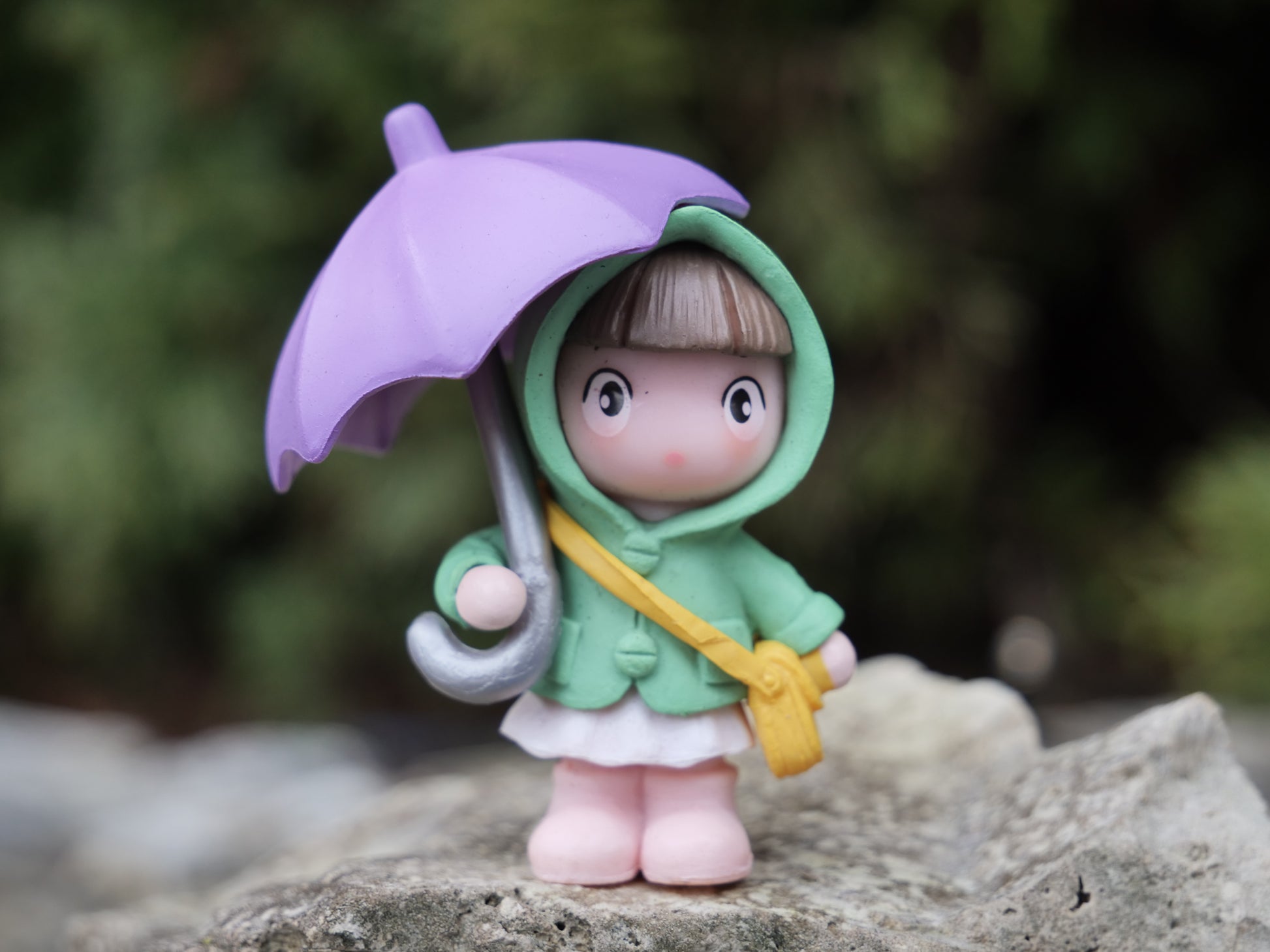 Teichfigur eines Mädchens mit grünem Mantel, weißem Rock und lilafarbenem Regenschirm, auf einem Stein platziert. Liebevolle Deko für asiatisch inspirierte Wassergärten.