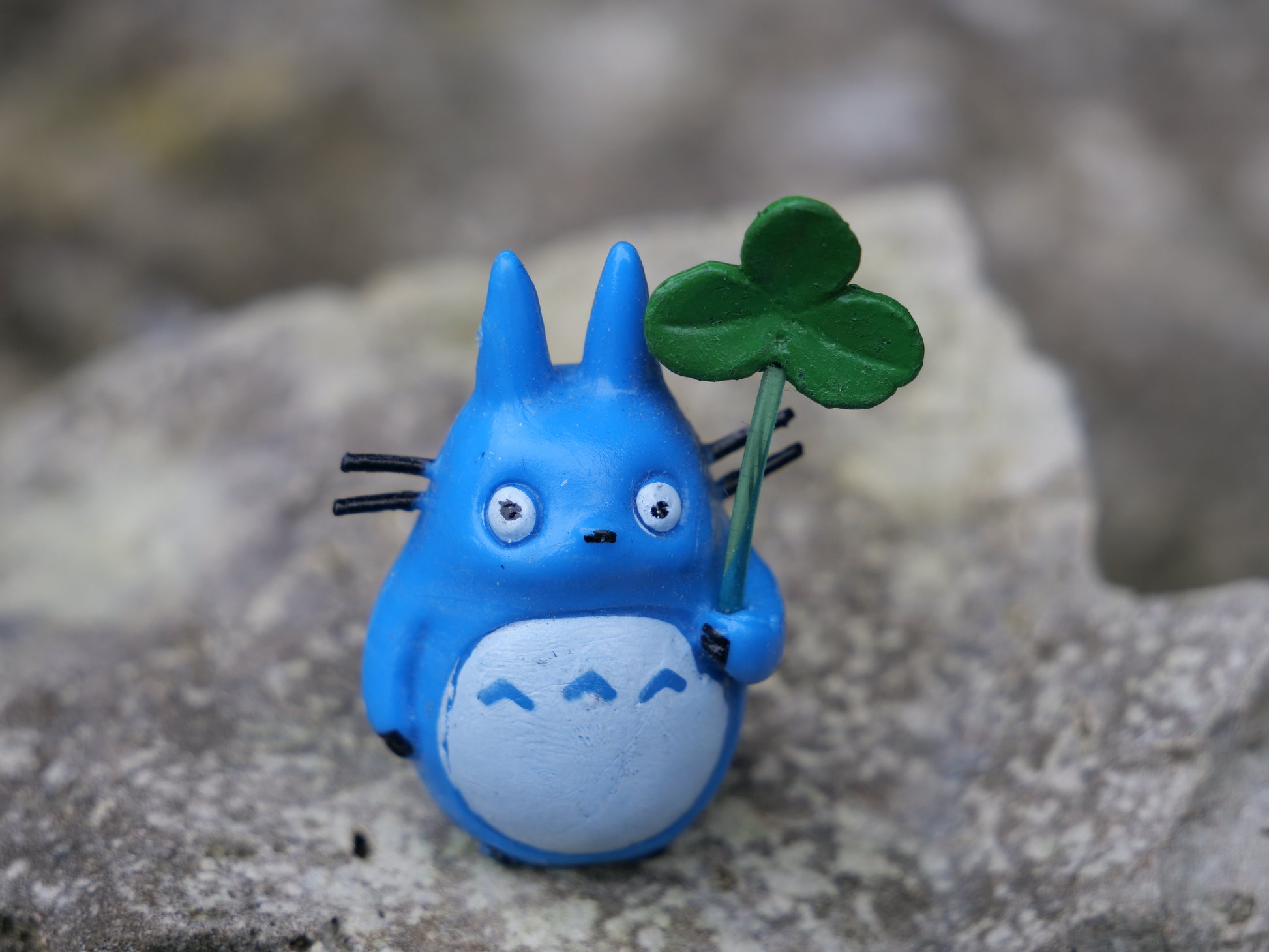 Detailaufnahme einer blauen Anime-Teichfigur mit Kleeblatt, auf einem Stein platziert. Farbige Gartendeko für kleine Wasserlandschaften und Mini-Oasen.