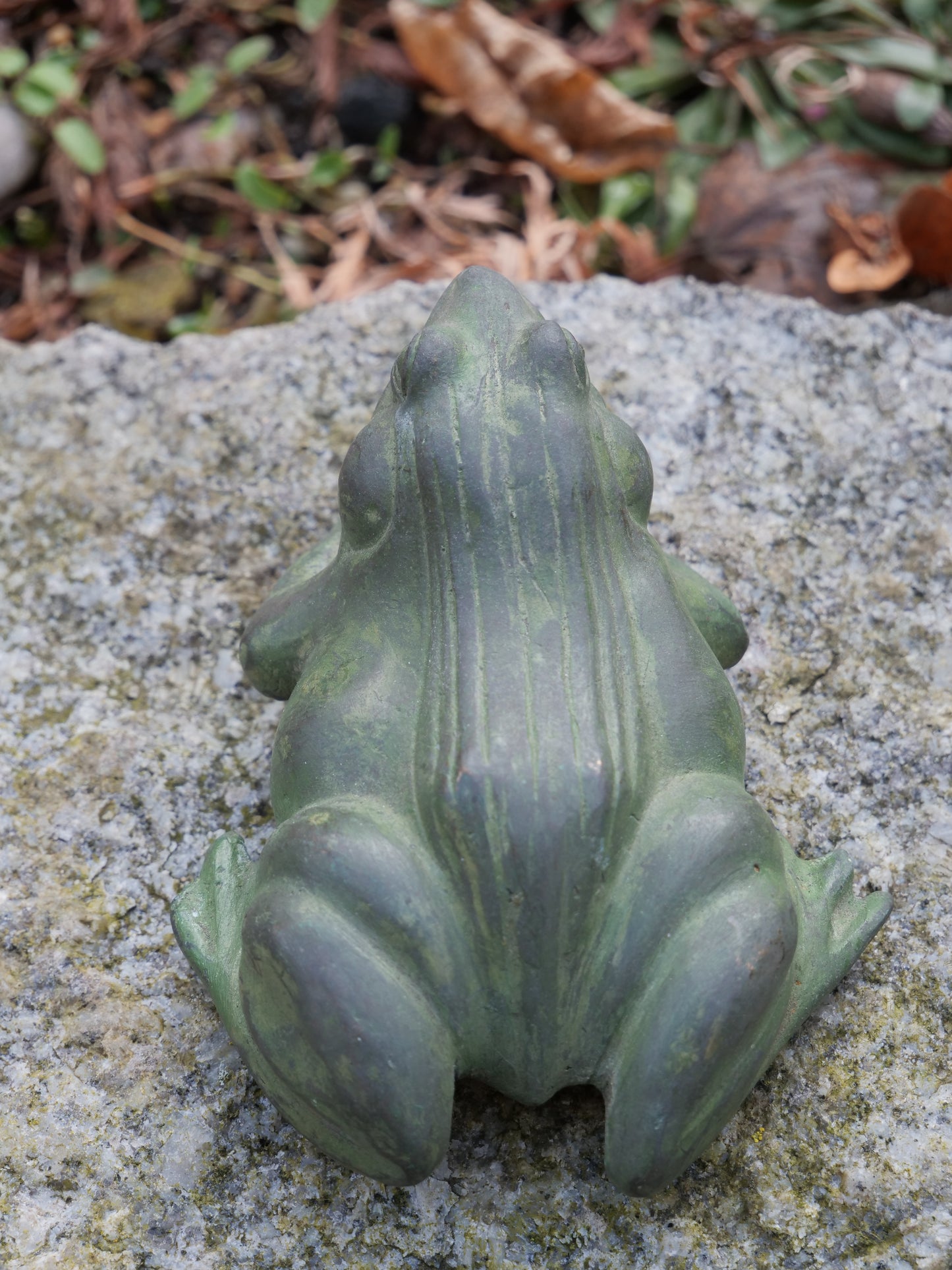 Messingfrosch von oben – Vogelperspektive auf eine kunstvoll gestaltete Froschfigur mit feiner Struktur, platziert auf Stein.