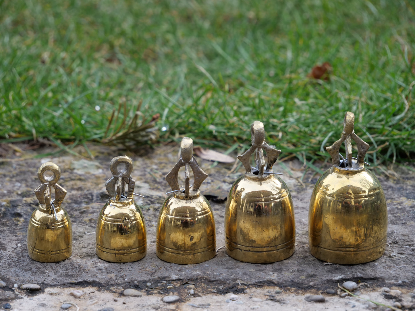 Fünf glänzende Messing-Glöckchen auf einem Stein, angeordnet in aufsteigender Größe mit kunstvollen Halterungen.