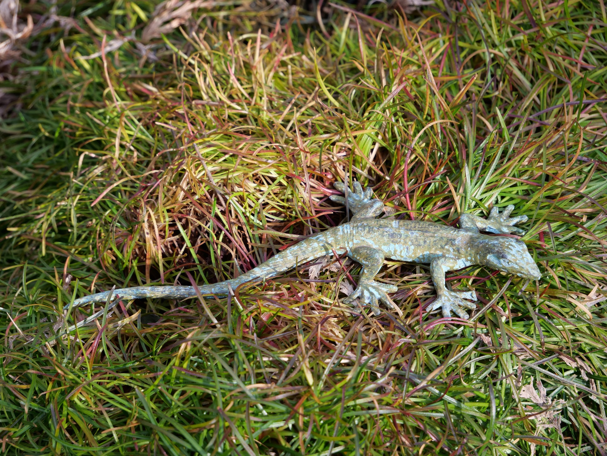 Messing-Gecko auf natürlichem Gras, exotische Tierfigur als Deko für Innen- und Außenbereiche.